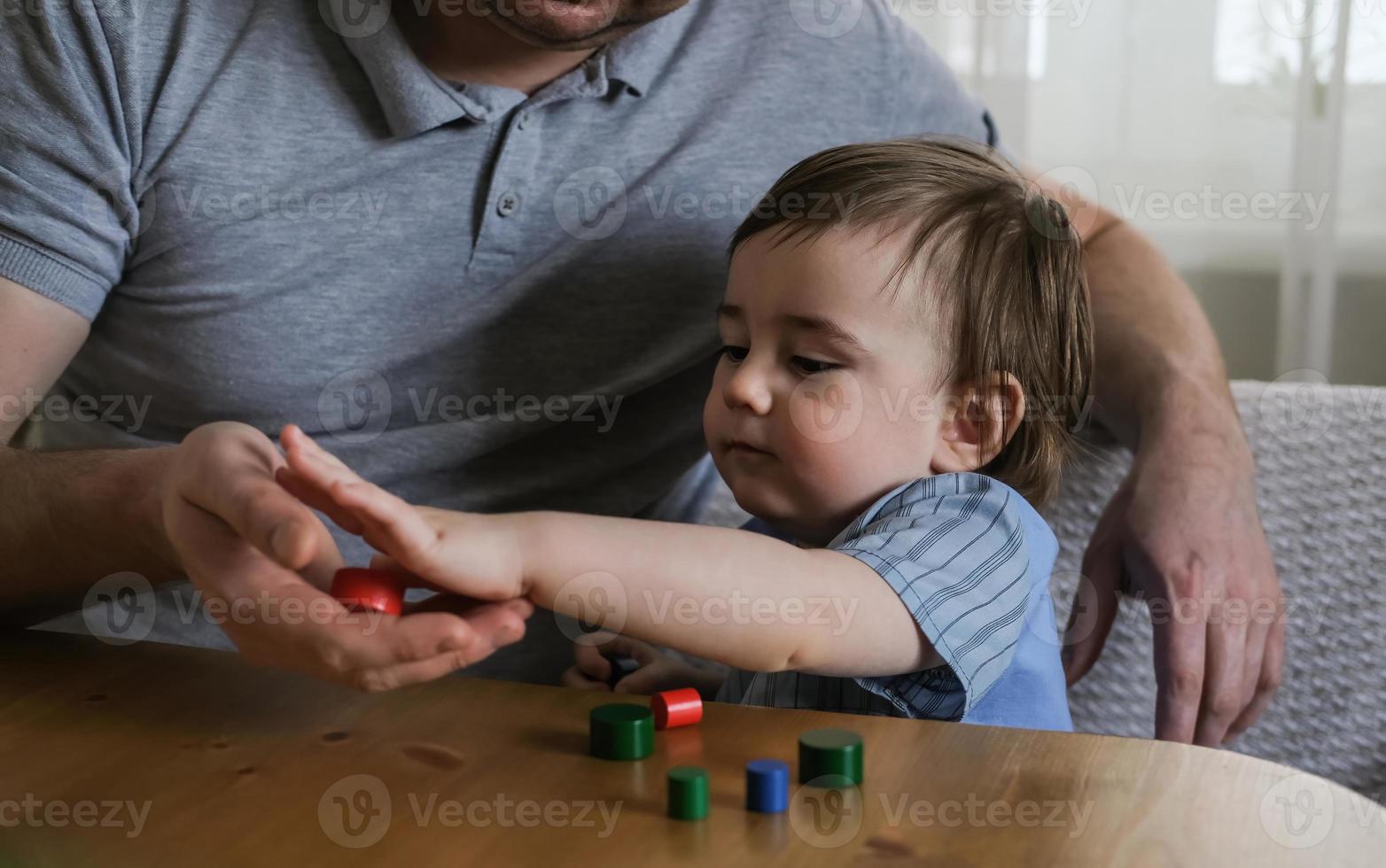 Dad and 1-year-old son play with wooden figurines at home. Development of fine motor skills and logical thinking of kids. Father's day concept photo