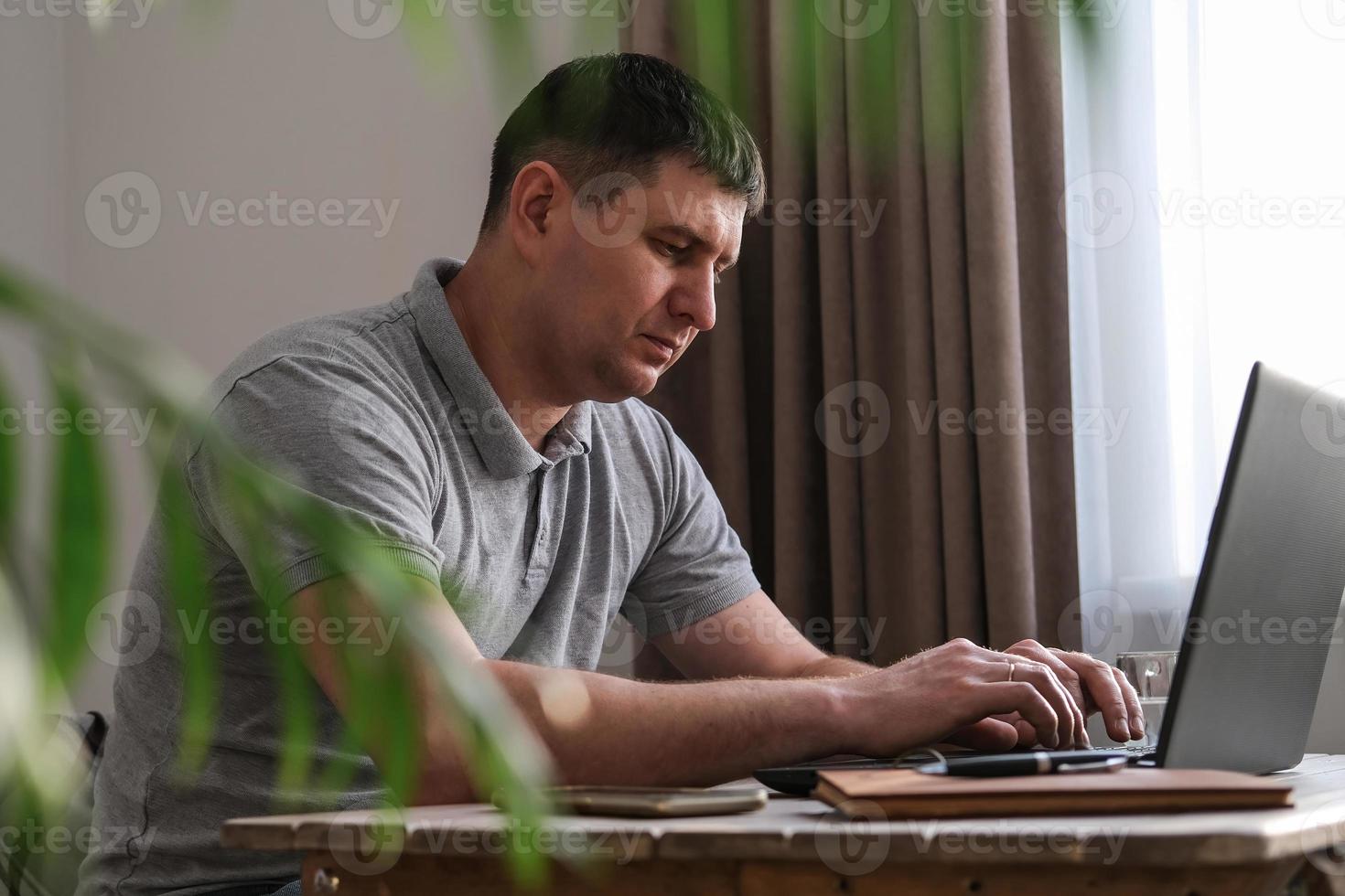 Serious young male programmer works on a laptop in a cozy home environment. Internet business, freelance photo