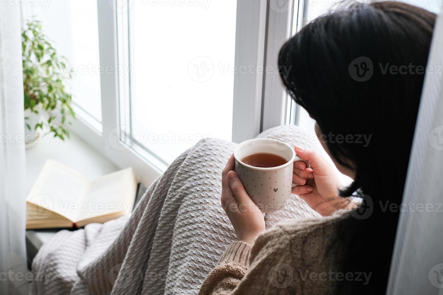 Young woman drinking tea while sitting on the windowsill photo