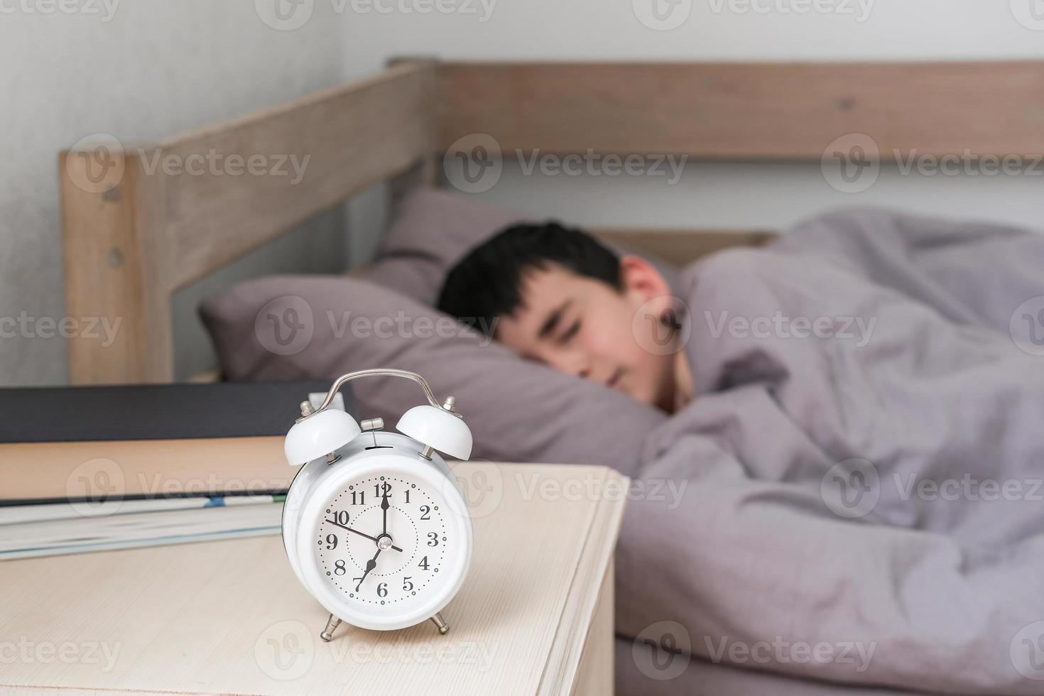 Alarm clock on the bedside table against the background of a boy sleeping under a blanket. Morning of the schoolboy photo