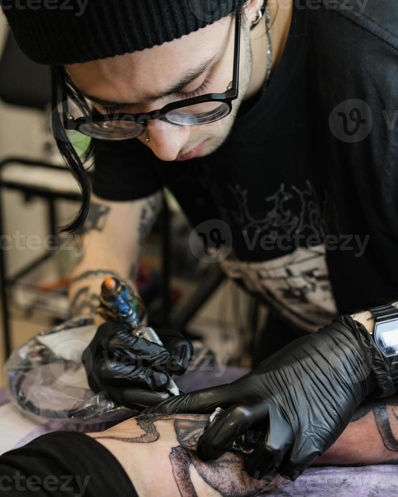 Professional tattoo artist stuffs a tattoo on the man's hand. Tattoo artist at work. Tattoo creation process. Art and creativity photo