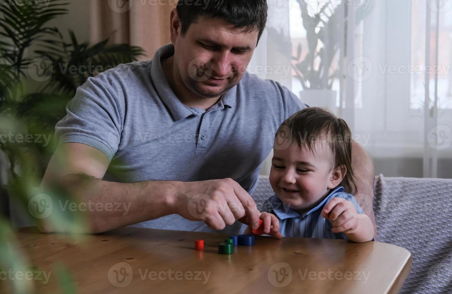 Dad and 1-year-old son play with wooden figurines at home. Development of fine motor skills and logical thinking of kids. Father's day concept photo