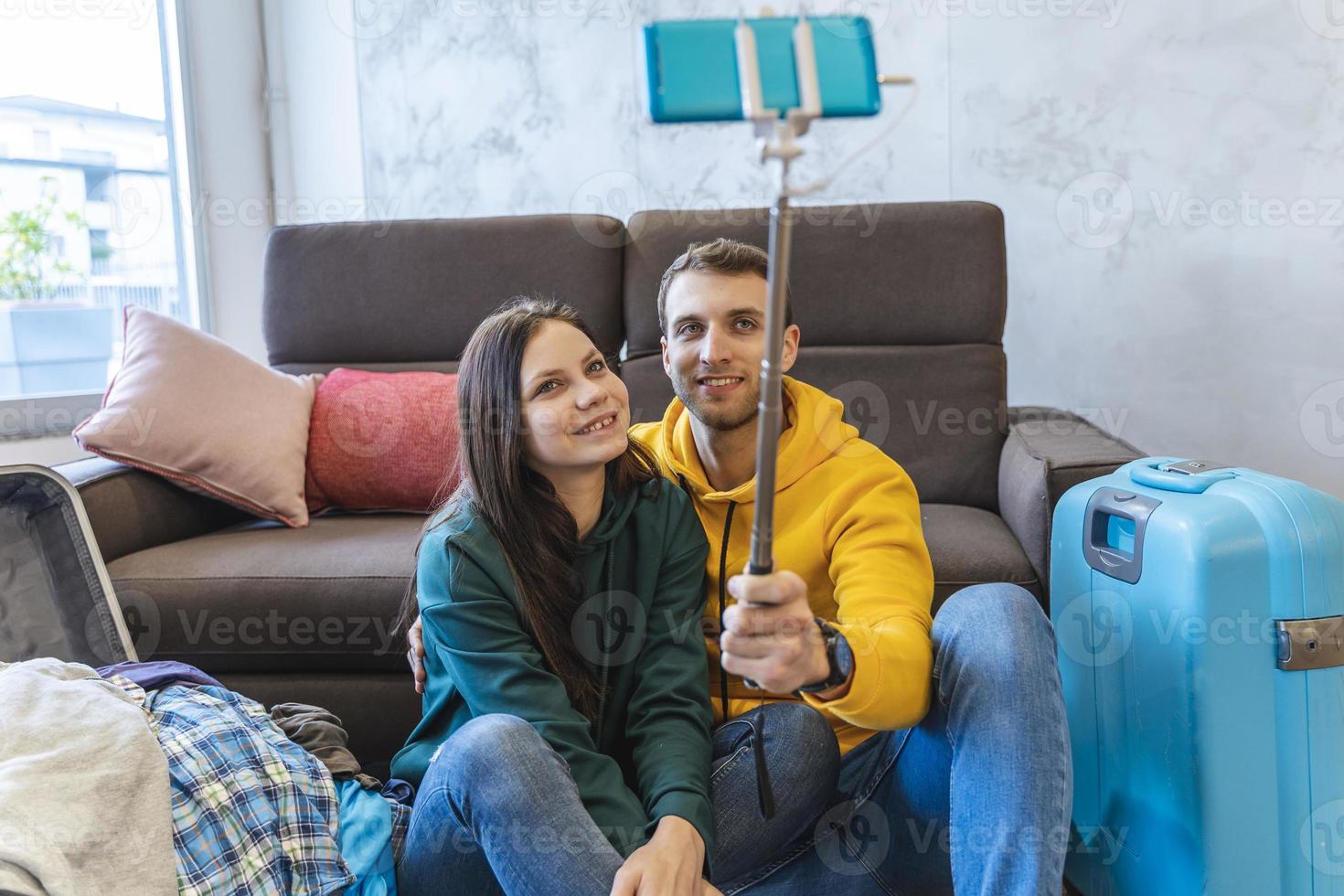 young couple sitting on the floor at home take a selfie between the suitcases photo