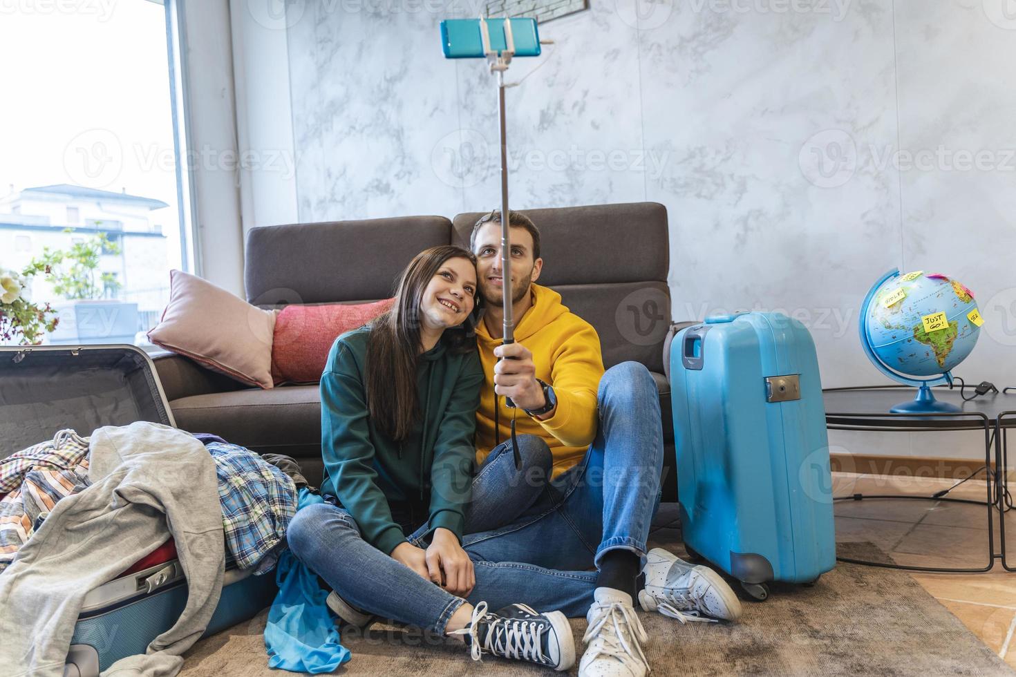 young couple sitting on the floor at home take a selfie between the suitcases photo