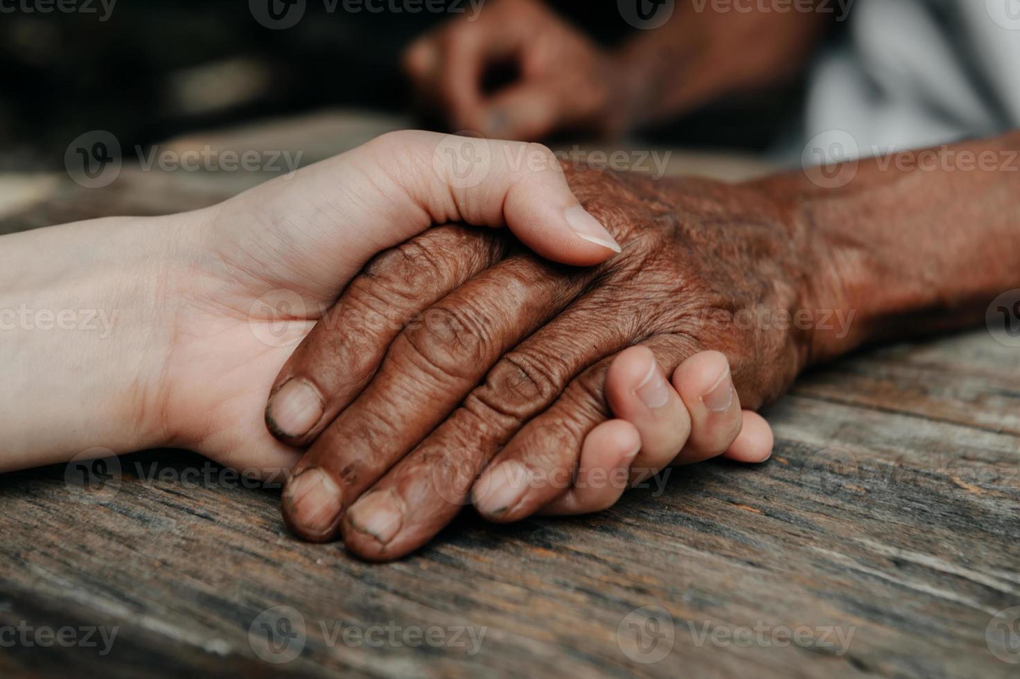 Hands of the old man and a woman hand on the wood table in sun light photo