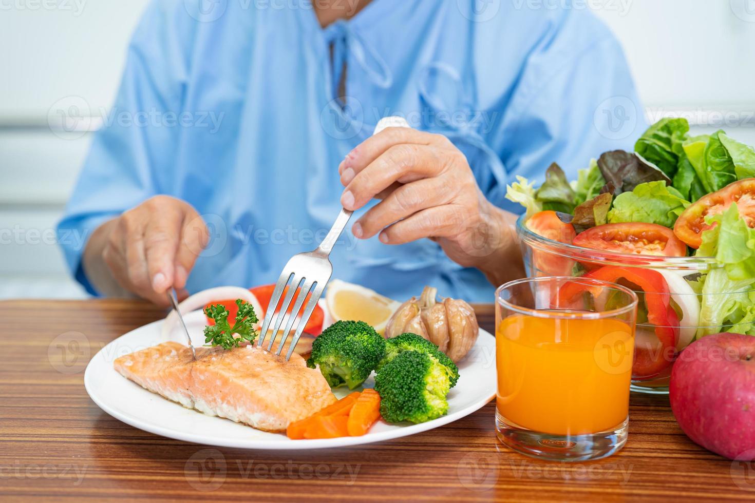 Asian senior or elderly old lady woman patient eating Salmon steak breakfast with vegetable healthy food while sitting and hungry on bed in hospital. photo