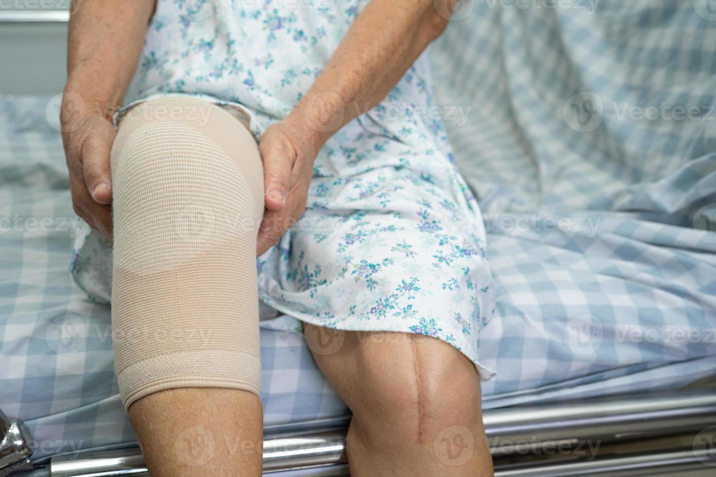 Asian senior woman patient with bandage compression knee brace support injury on the bed in hospital ward, healthy strong medical concept. photo