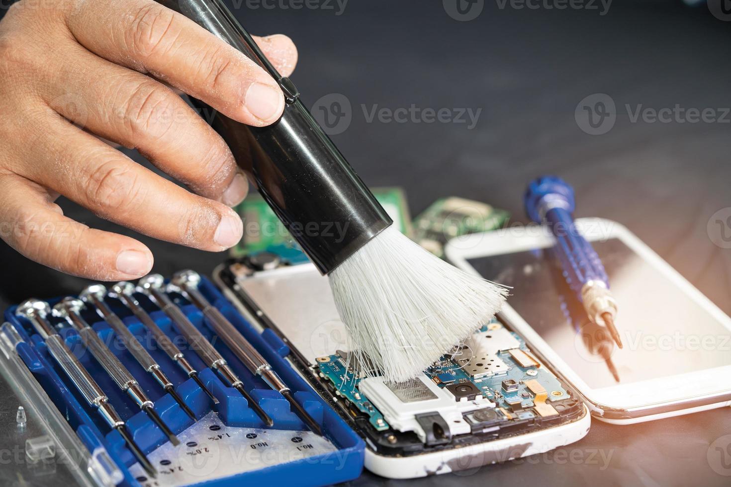 Asian technician repair and cleaning dirty micro circuit main board of smartphone electronic technology with brush, hardware, mobile phone, upgrade concept. photo