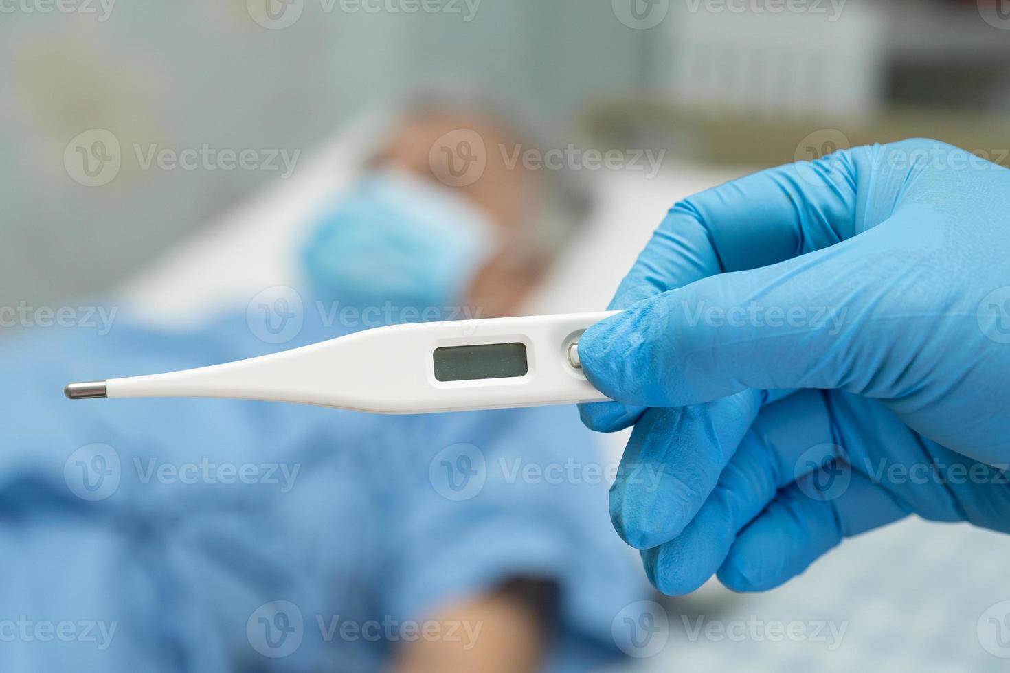 Doctor holding digital thermometer to measures asian elderly woman patient wearing a face mask have a fever in hospital, healthy strong medical concept. photo