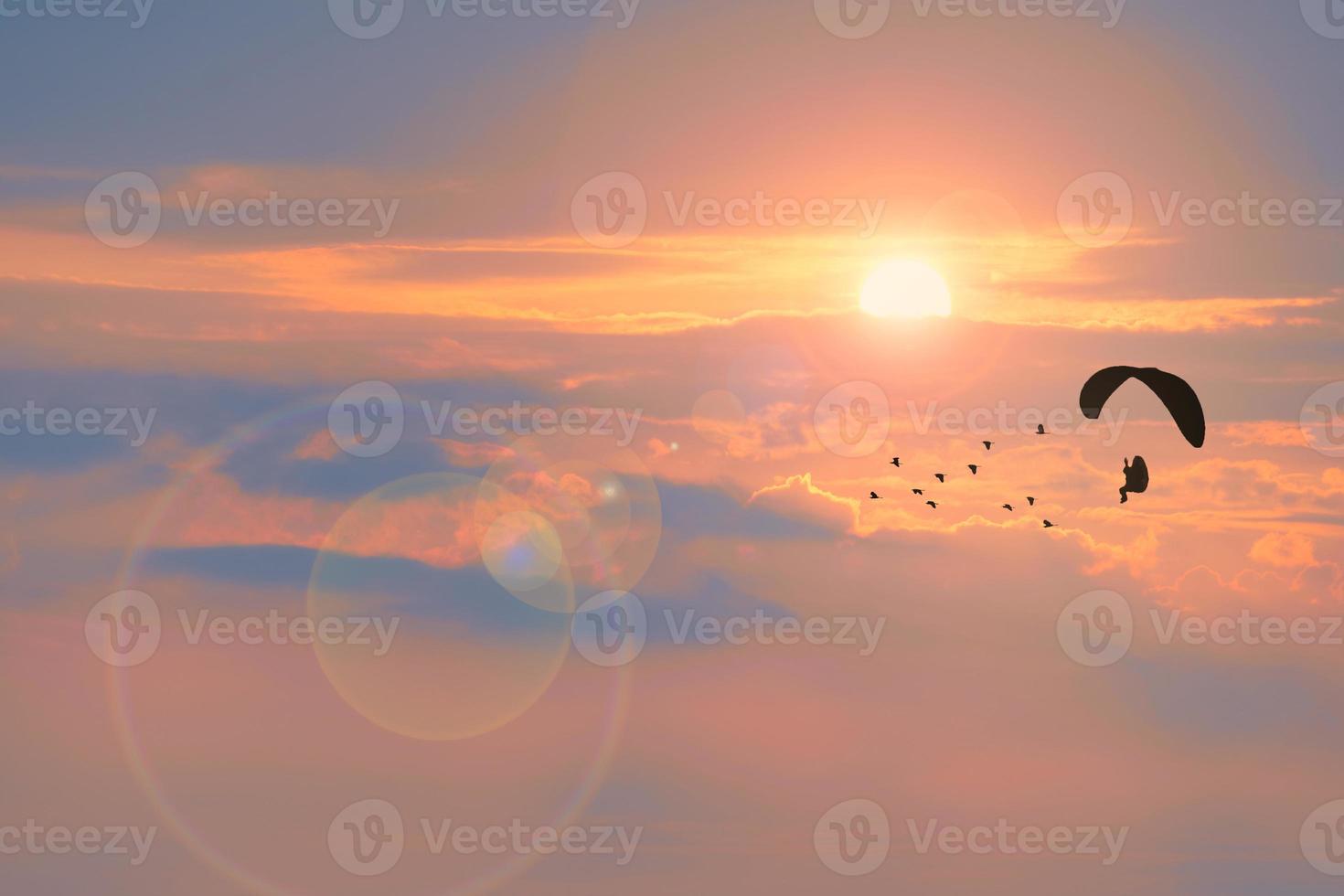 silhouette paramotor flying follow birds and sunset cloud background with fog over on the top mountain photo