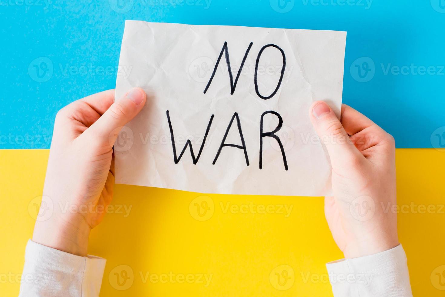 The concept of stop the war in Ukraine. Childrens hands hold a poster with the inscription no war on the background of the Ukrainian flag. Top view. photo