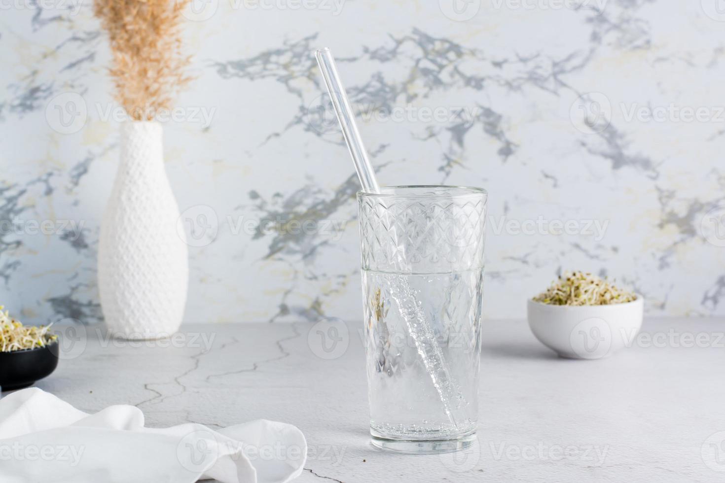 un vaso de limpiar agua y un vaso Paja para Bebiendo en un ligero mesa. dieta orgánico estilo de vida foto