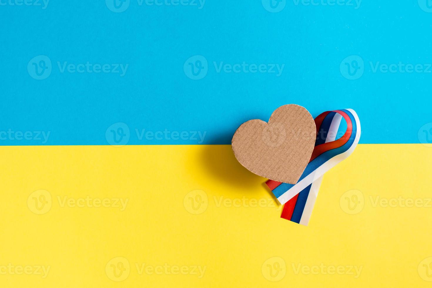 The concept is no war in Ukraine. Cardboard heart and ribbon of the Russian flag on the background of the Ukrainian flag. Top view. photo