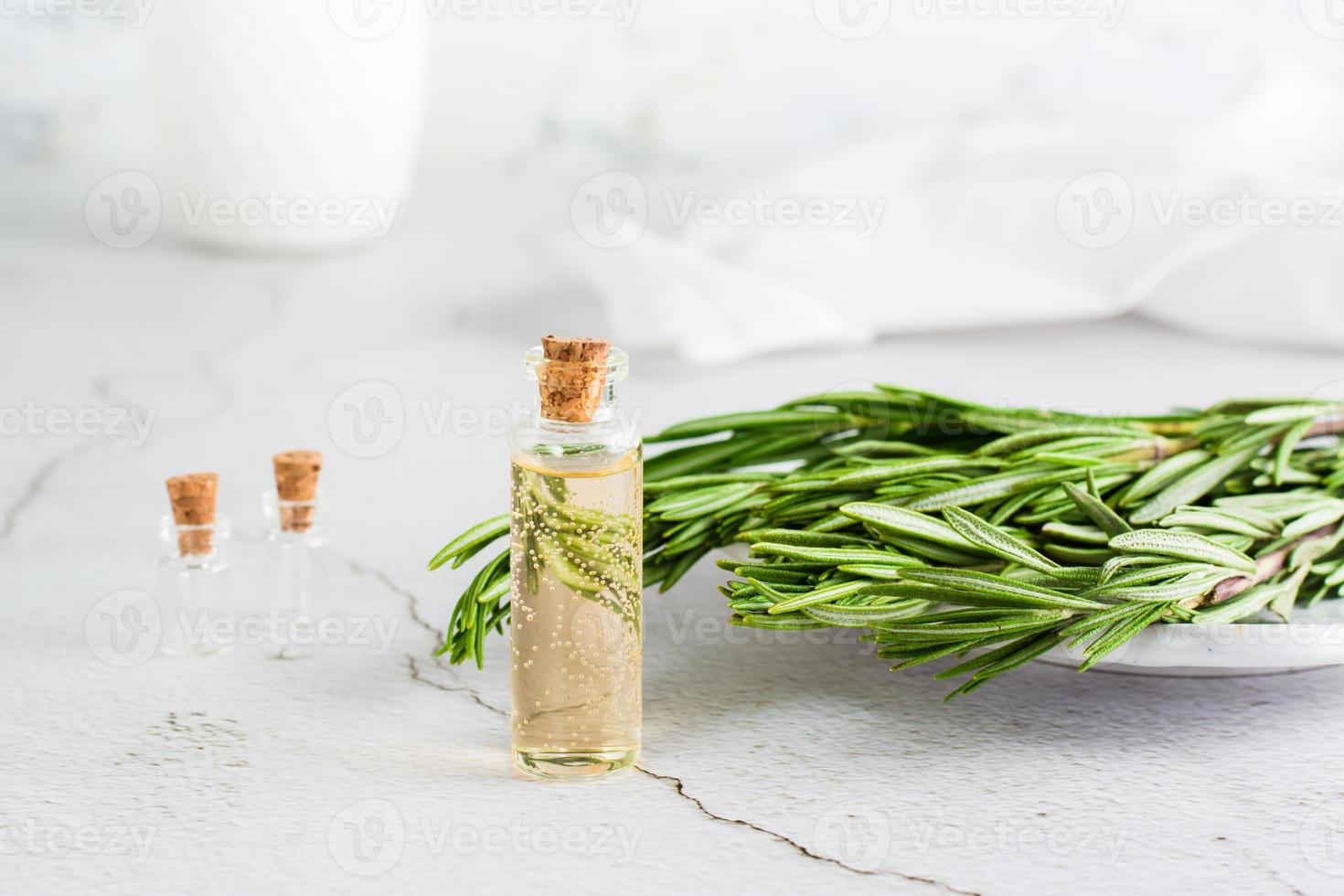 A bottle of rosemary essential oil and herb branches on a plate on the table. Organic aromatic natural remedy. photo