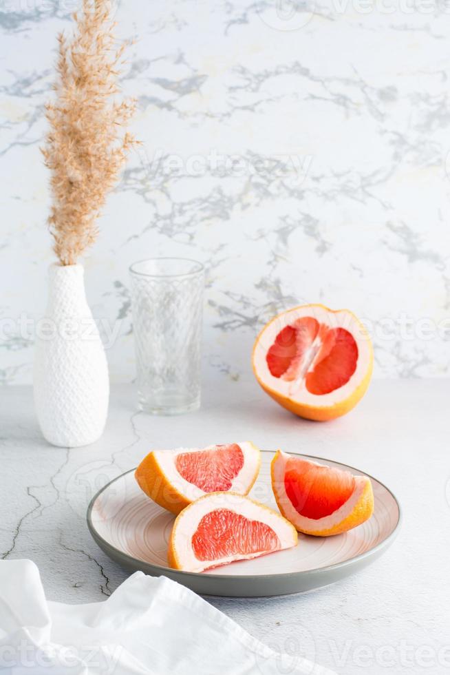 Ripe grapefruit slices on a plate on a light table. Sustainable lifestyle. Vertical view photo