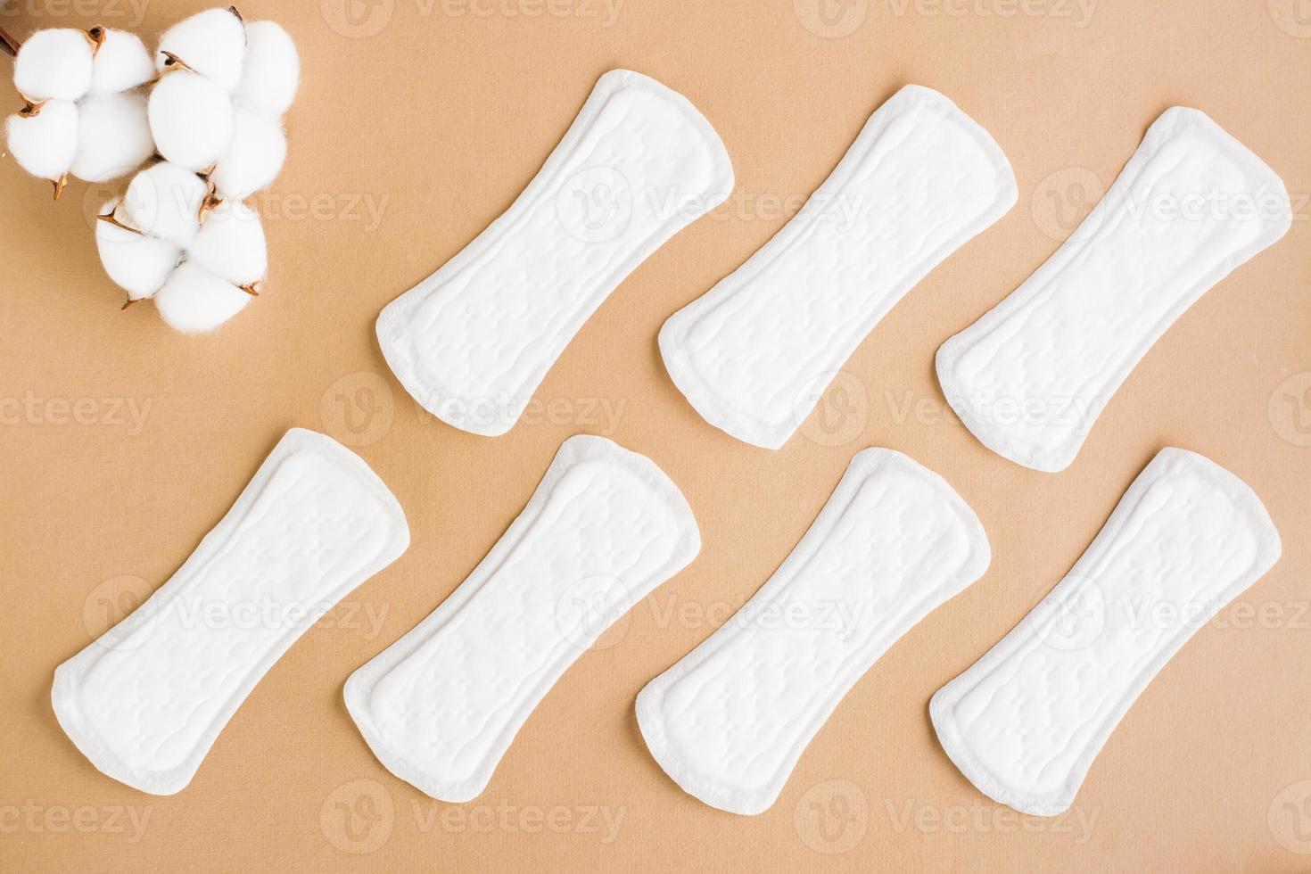 A pattern of clean disposable sanitary pads and a branch of cotton on a beige background. Women's health and comfort concept. Top view photo