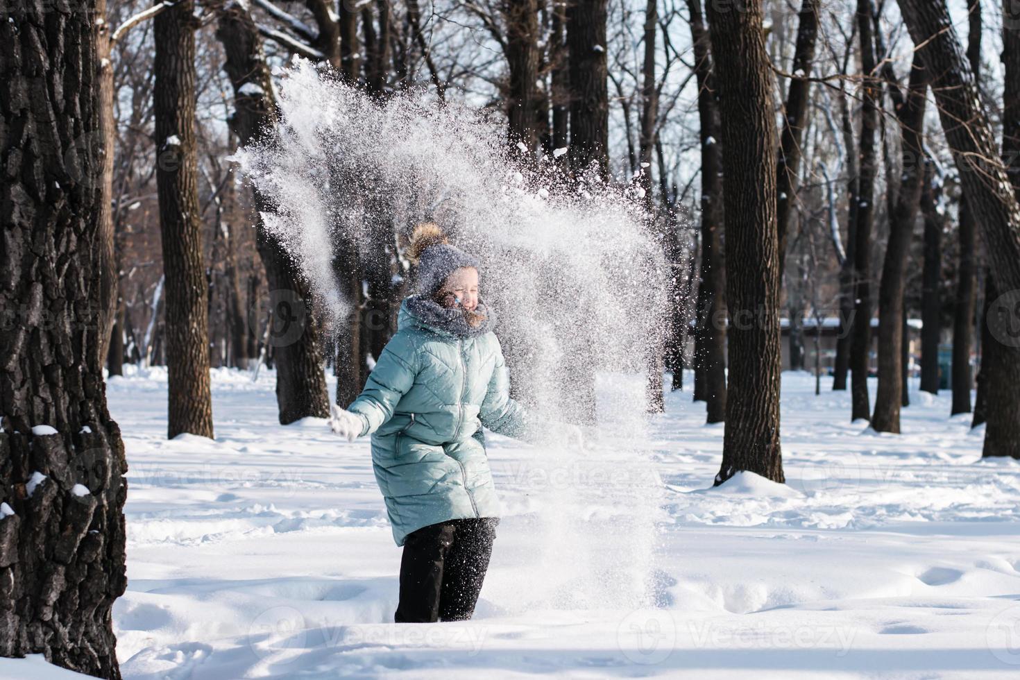 Happy girl in warm clothes throws snow in the winter forest. Walk outdoors. photo