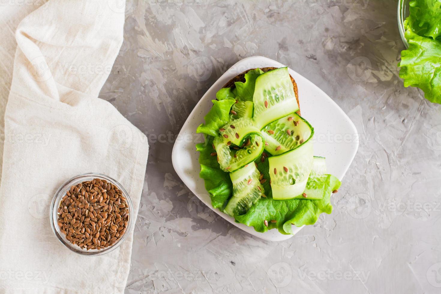 Appetizing bruschetta from rye bread, lettuce, cucumber and flax seeds on a plate and a bowl with grains on the table. Healthy diet food. Top view. photo