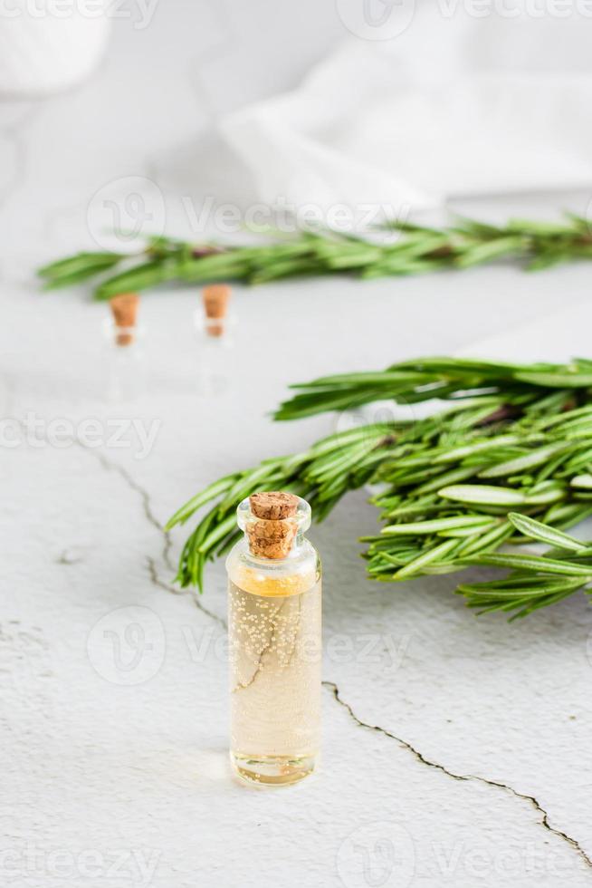 A bottle of rosemary essential oil and herb branches on a plate on the table. Organic aromatic natural remedy. Vertical view photo