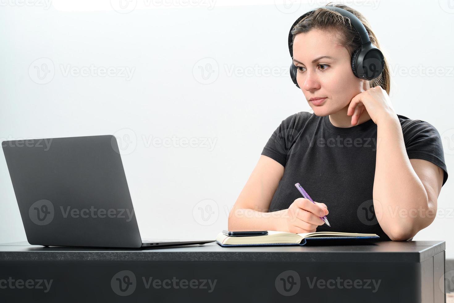 ocupado joven mujer en auriculares trabajando en computadora portátil, haciendo vídeo llamada y haciendo notas en computadora portátil, trabajo y estudiar en línea. foto