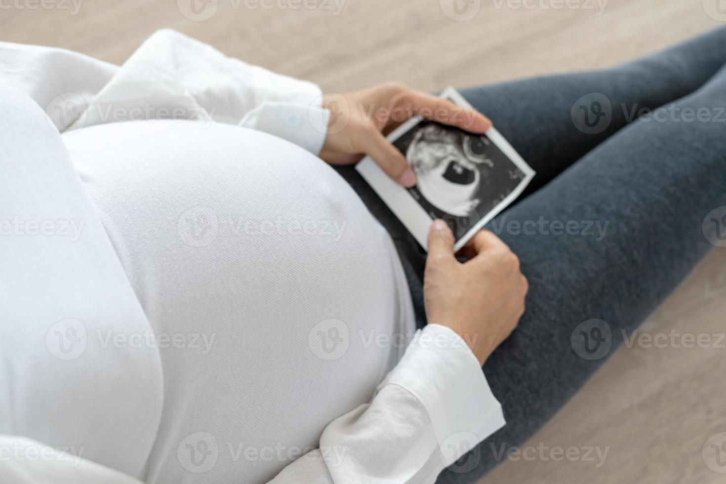 pregnant woman is looking at an ultrasound photo of fetus. Mother gently touches the baby on stomach. Happy, family, growth, pregnancy, enjoyment , prepare newborn, take care, healthcare, tummy.