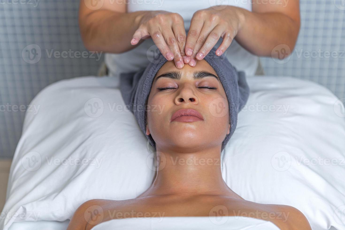 esteticista dando un facial masaje con crema en un relajado mujer cara a salud spa foto