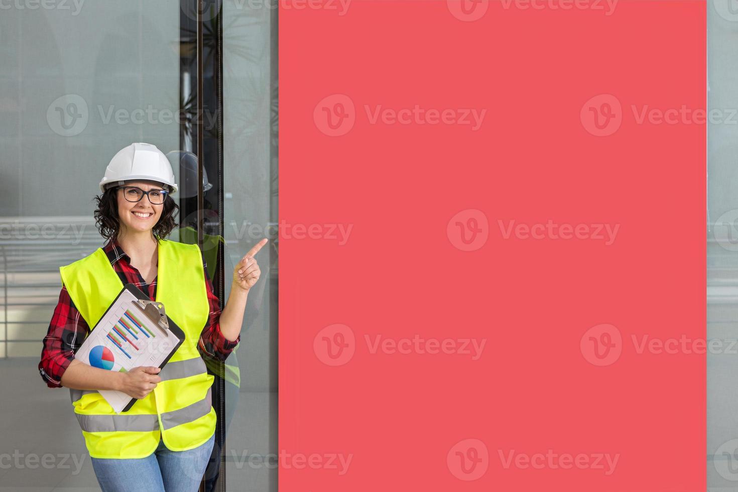 mujer trabajador con un chaleco y casco señalando un rojo póster foto