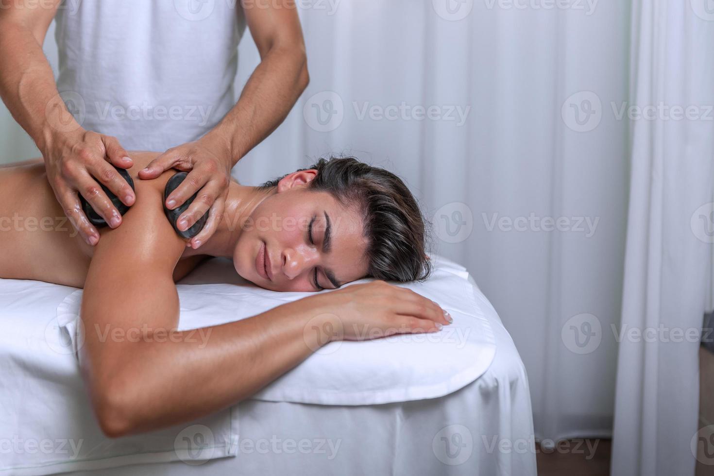 cerca arriba ver de un mujer recepción un brazo y hombro masaje con piedras por profesional masajista en spa salón foto