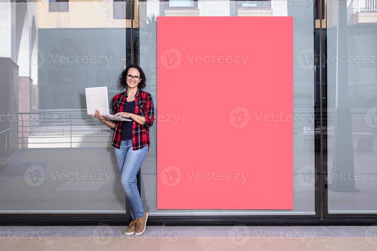 Saleswoman facing the camera with a laptop next to a shop window outdoors photo