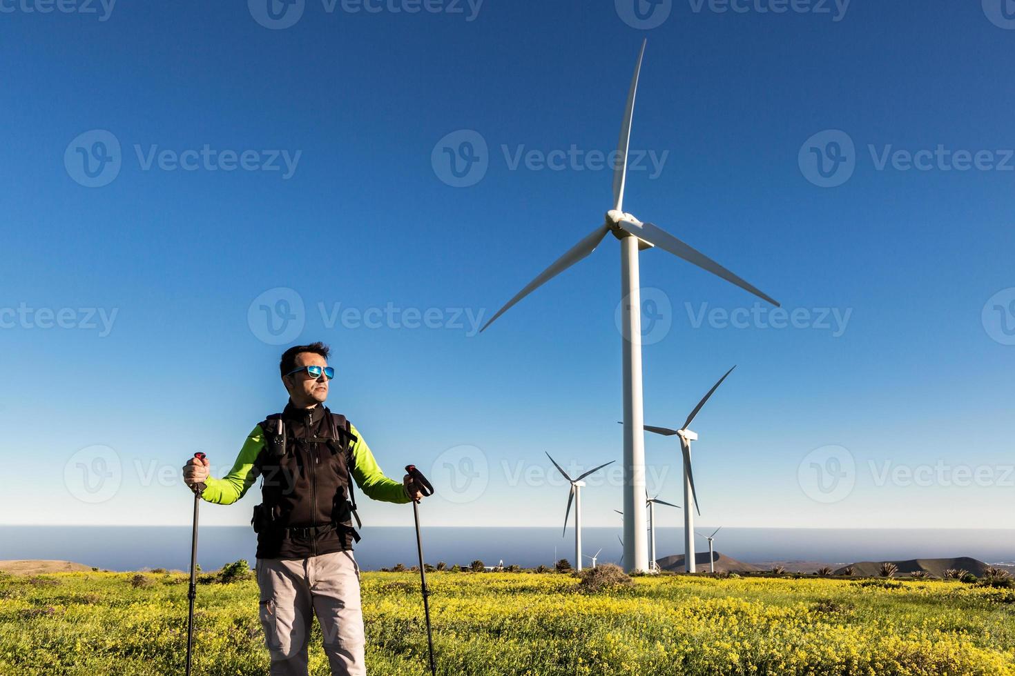 Male hiker with trekking poles standing in field with windmills photo