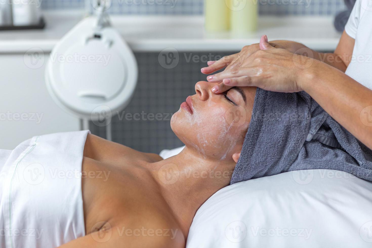 lado ver de un cosmetólogo aplicando crema en cara de mujer en el piel cuidado tratamiento en spa salón foto