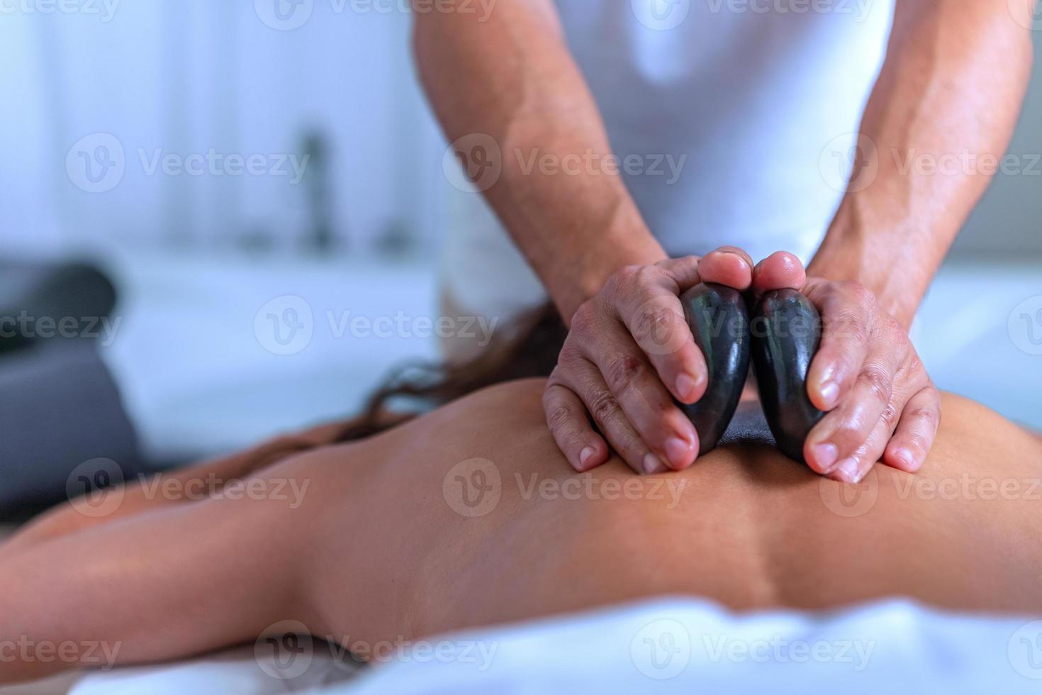 cerca arriba de manos de un profesional masajista haciendo un espalda masaje con piedras a un mujer en spa salón foto