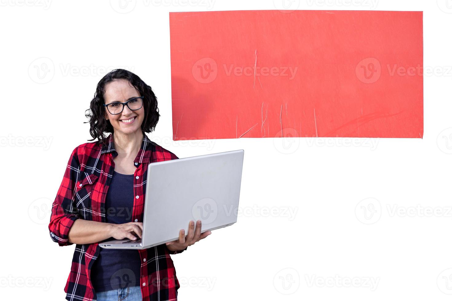 Smiling woman with glasses holding a laptop standing in front of a red banner photo