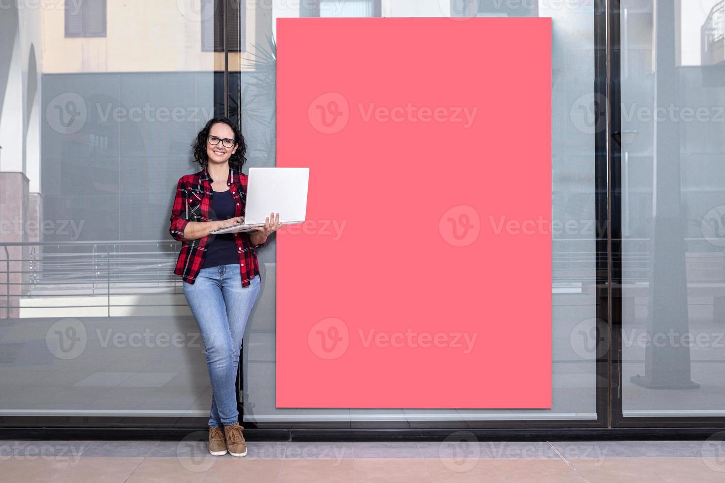 Woman standing while using a laptop next to a shop window photo