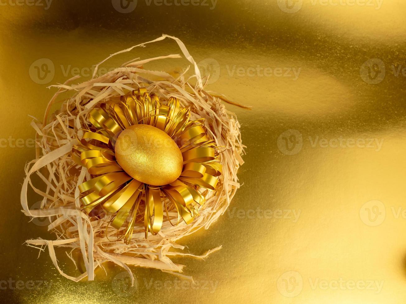 One Easter egg, painted gold and black, lies in a nest on a glittering gold background photo