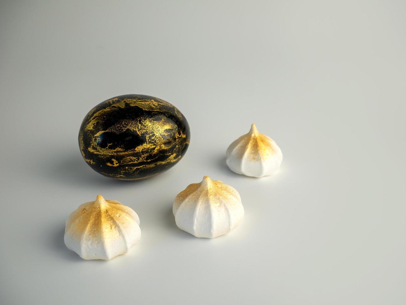 Easter egg painted in gold and black on a light background with meringues photo