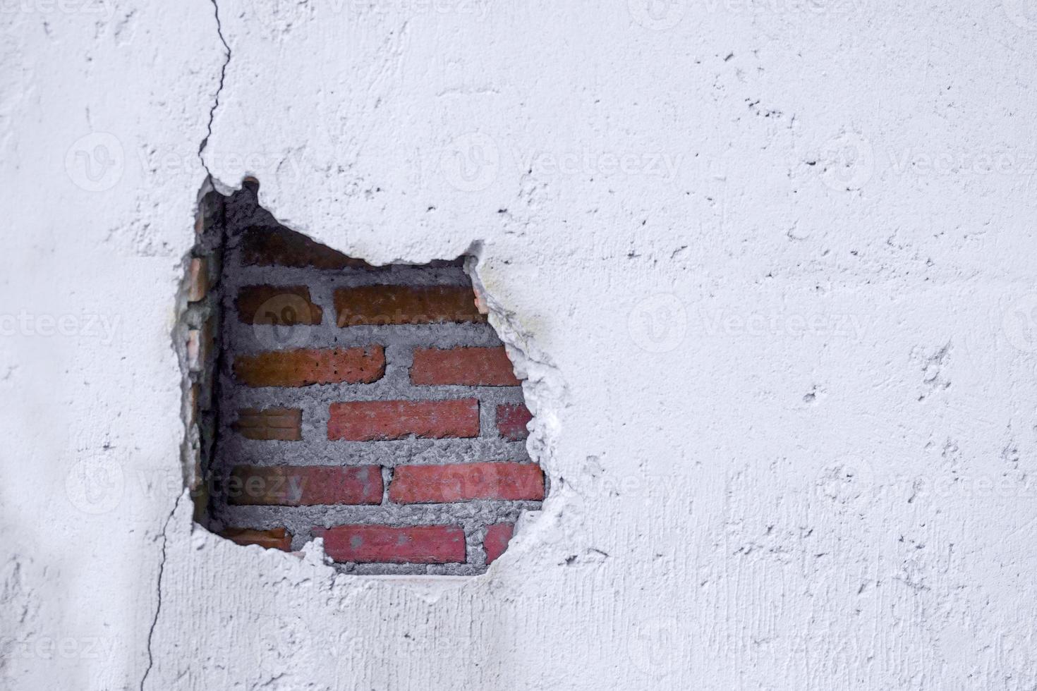 agujero en roto pared y antiguo ladrillos en blanco antecedentes. grande grieta en el pared de un antiguo ladrillo casa, desmoronándose yeso y roto, agrietado ladrillos foto