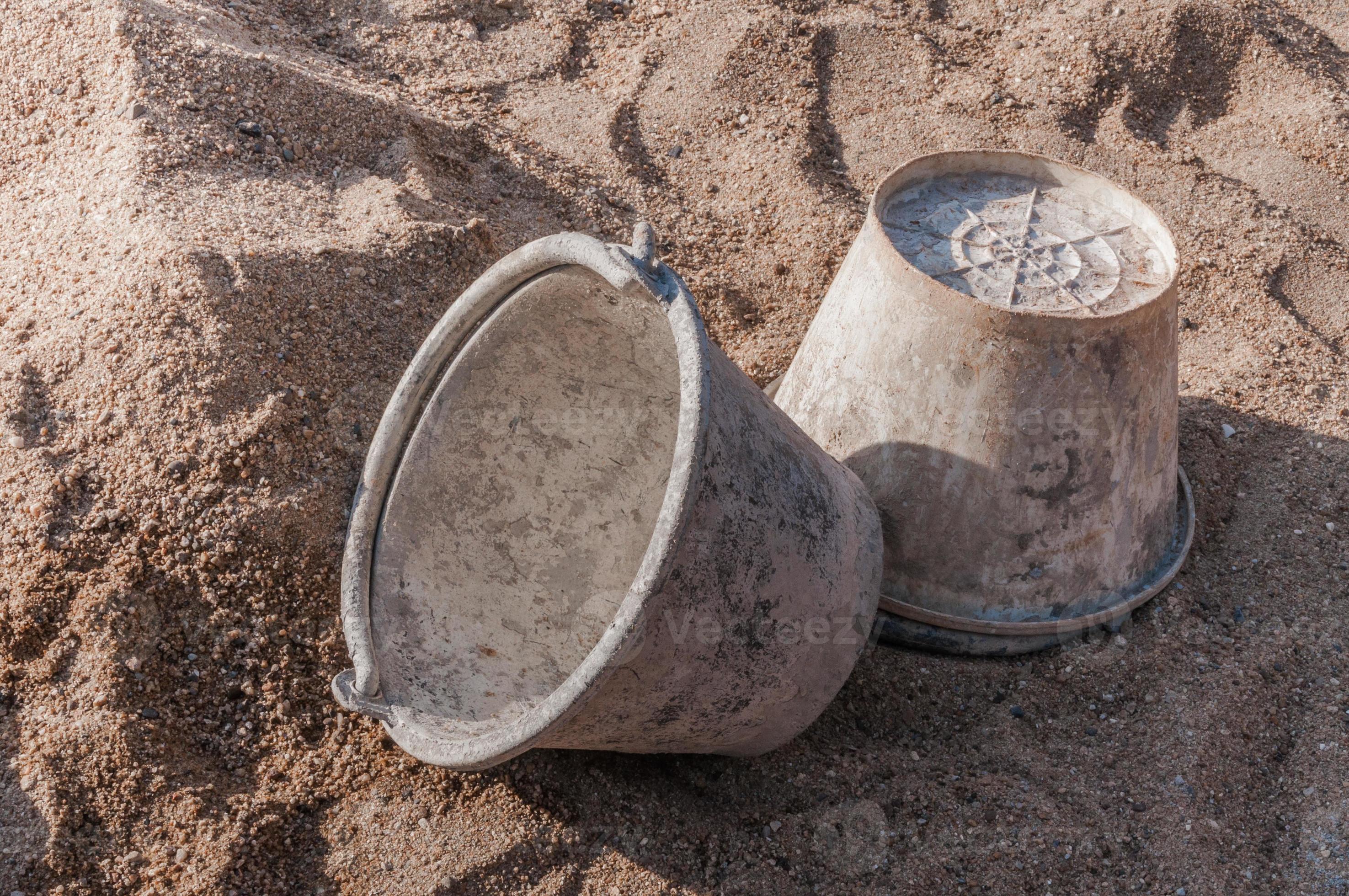 Plastic bucket with cement placed on on the sand at construction site