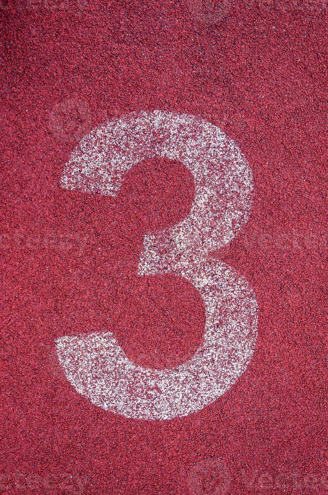 Number three on running track. White track number on red rubber racetrack, texture of running racetracks in stadium photo