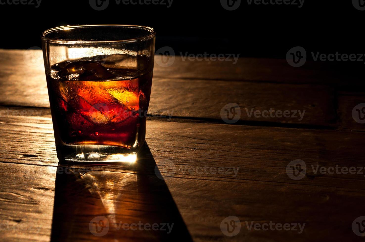 Cola with whiskey and ice on a wooden table background photo