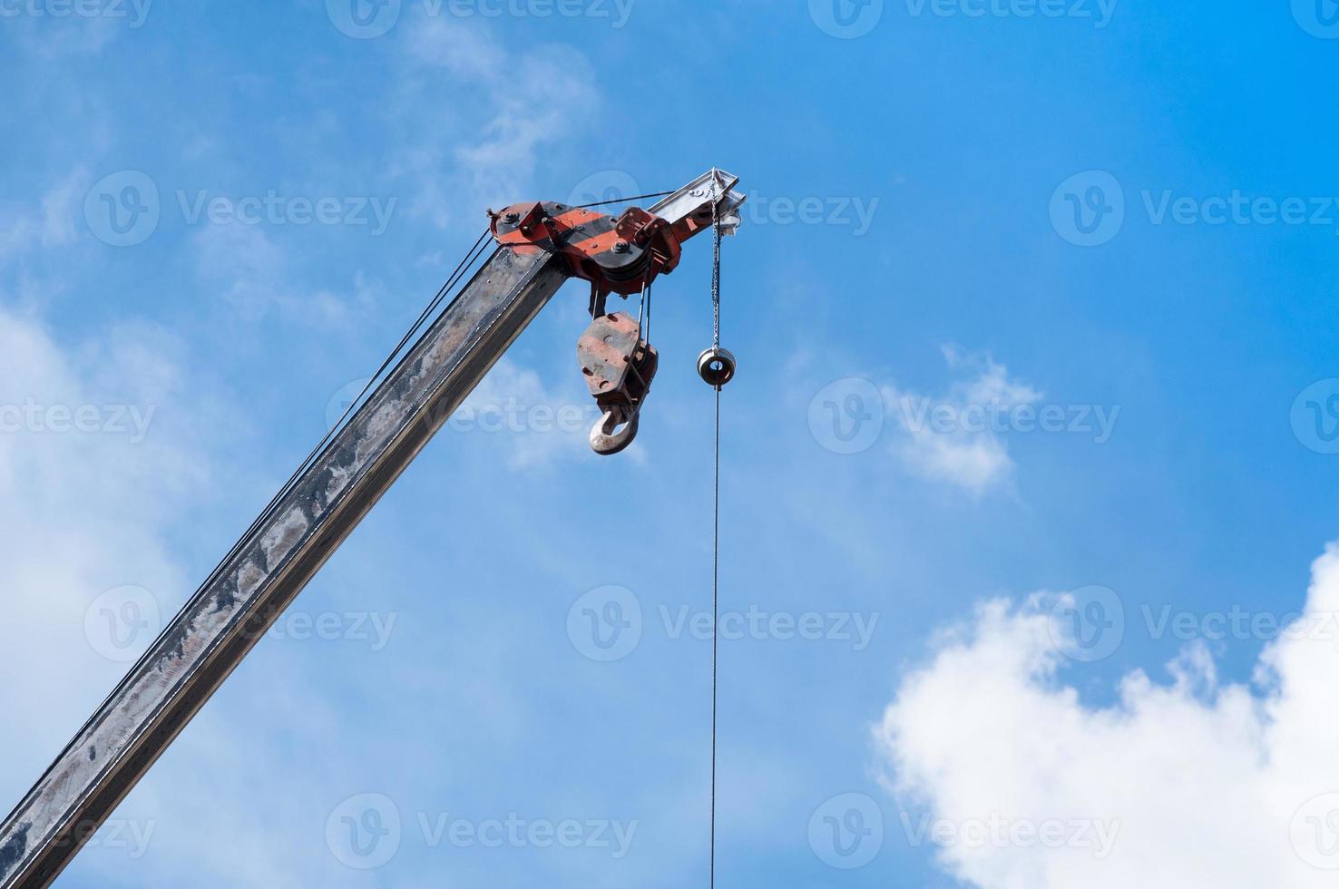 Mobile crane boom with hook hanging by wire cable background blue sky,close up photo