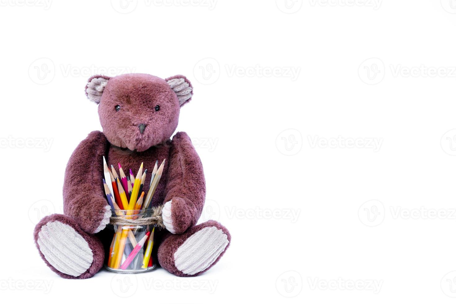 marrón osito de peluche oso muñeca sentado con vistoso lapices en un vaso aislado en blanco, para educación espalda a colegio antecedentes foto