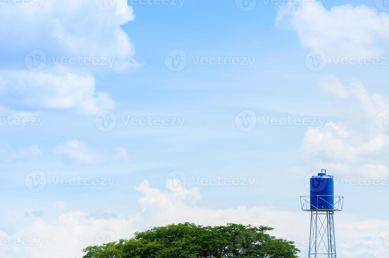 A plastic blue water tank on the tower in park photo