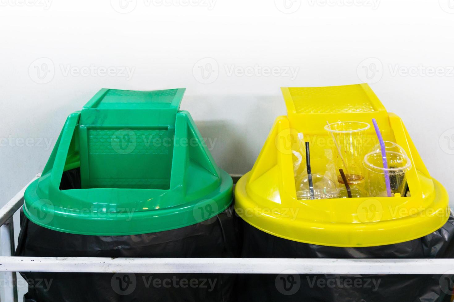 Yellow and green plastic trash recycle bin on white wall photo