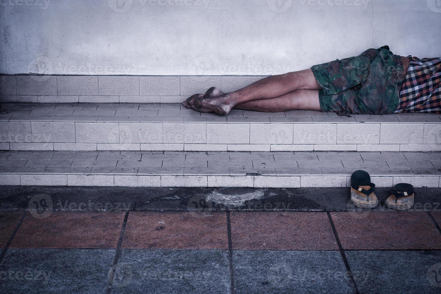 Homeless man dirty sleeps on the street in the shadow of the building. photo