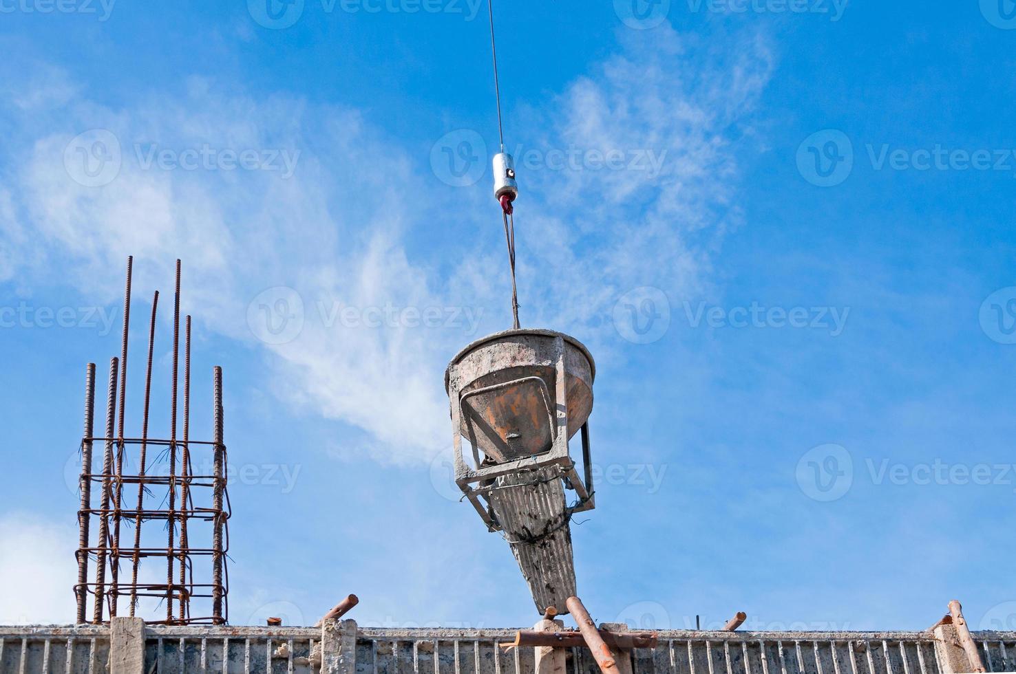 Cement or concrete bucket hanging on wire at construction site with blue sky background photo