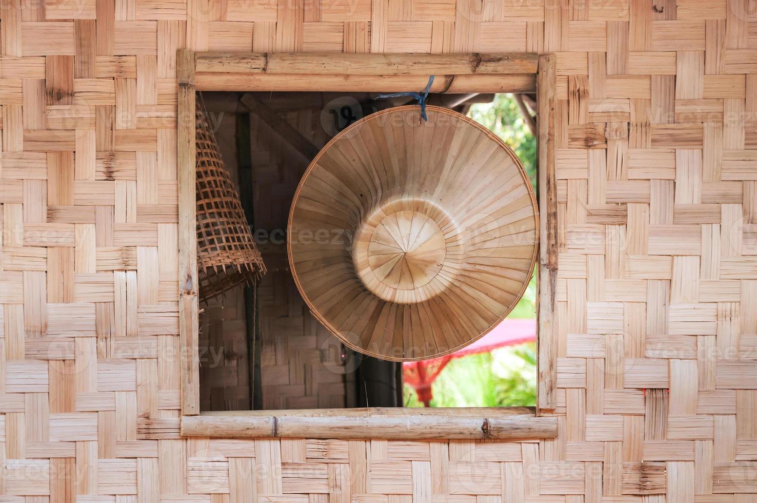 Beautiful local handmade Asian hat on surface of bamboo hanging on the window of a bamboo house. photo