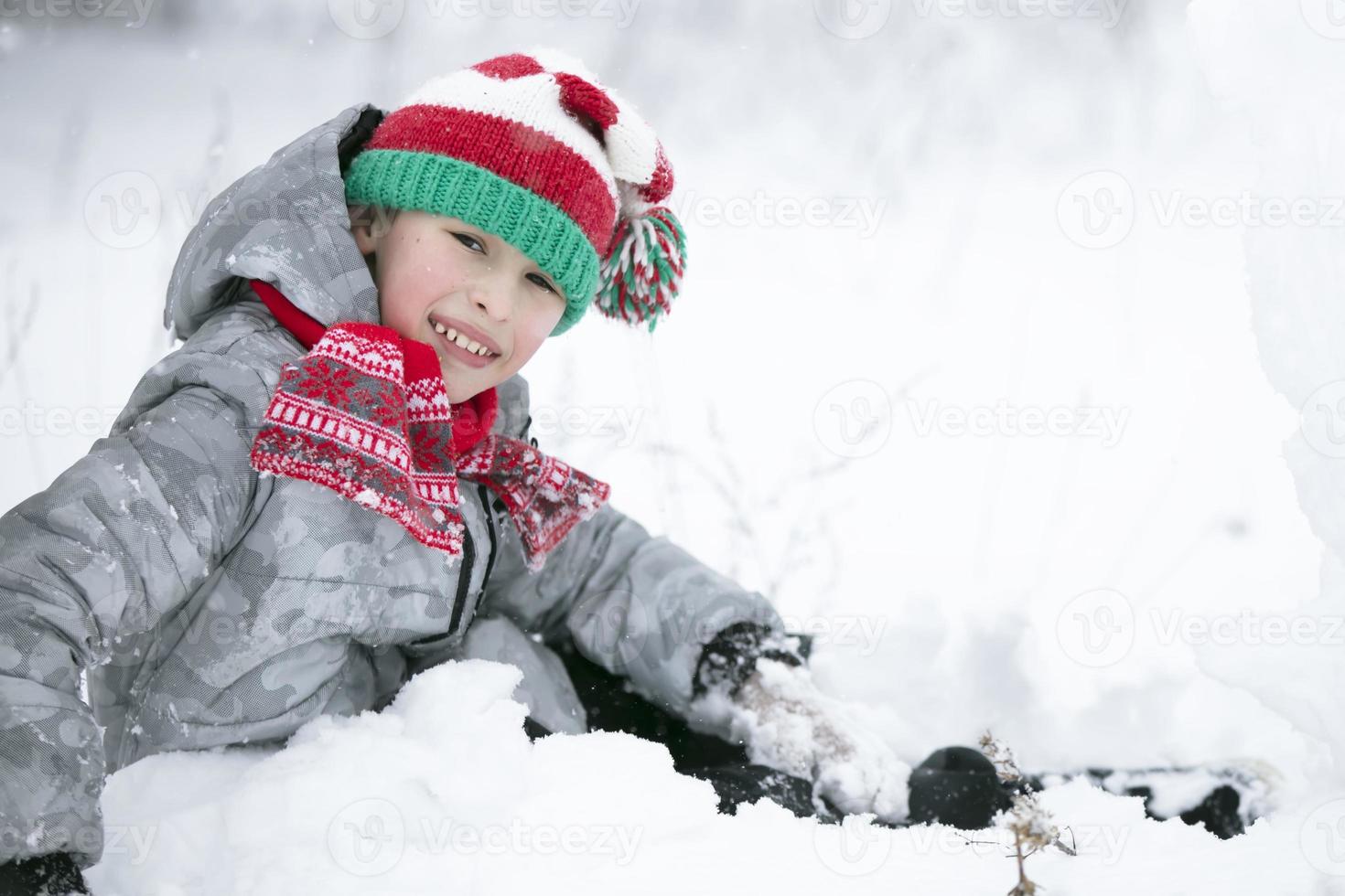 A little boy in a red knitted hat plays in the snow. photo