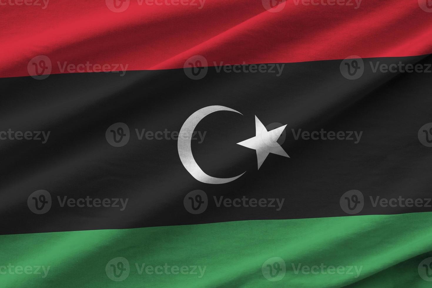 Libya flag with big folds waving close up under the studio light indoors. The official symbols and colors in banner photo