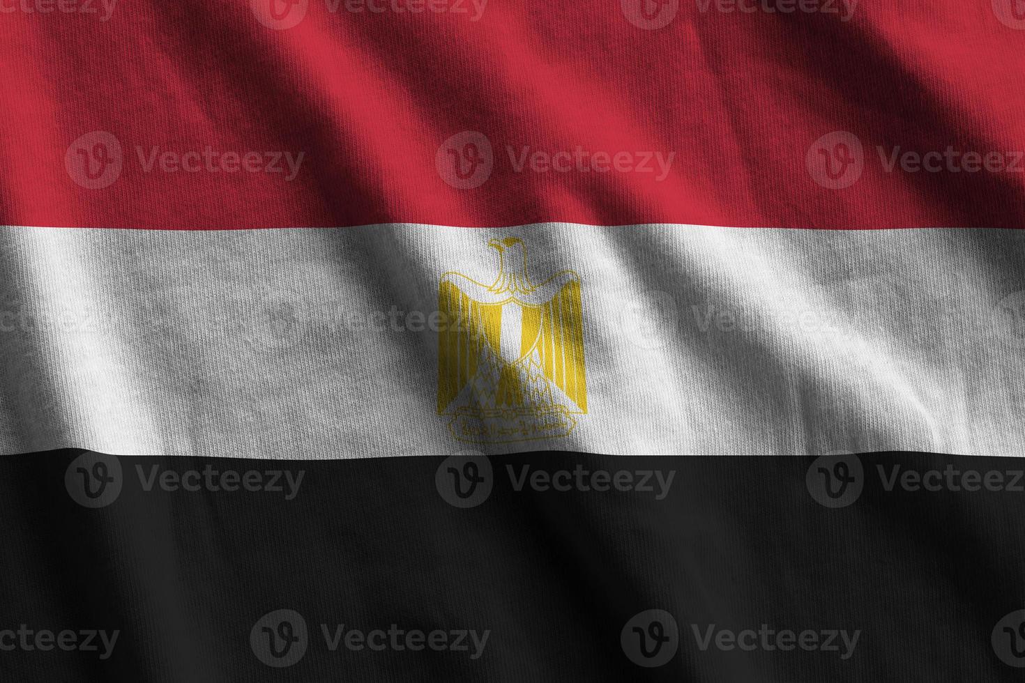 Egypt flag with big folds waving close up under the studio light indoors. The official symbols and colors in banner photo